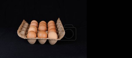Photo for Egg carton with fourteen eggs, with a hole where one egg is missing. The eggs are brown, packed in recycled cardboard. With black background - Royalty Free Image