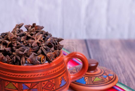 Photo for Clay jar containing star anise on an old wooden table and with a tablecloth from the highlands of Peru - Royalty Free Image