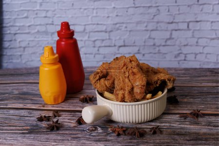 Photo for Fried chicken with ketchup and mustard in a yellow terracotta bow with star anise on an old wooden table - Royalty Free Image