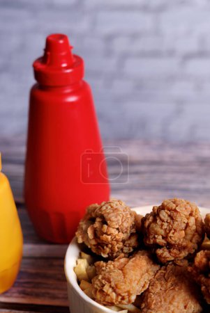 Photo for Fried chicken with ketchup and mustard in a yellow terracotta bow with star anise on an old wooden table - Royalty Free Image