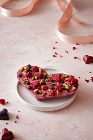 Photo for Valentine's day heart-shaped chocolate with nuts and berries on a light background. Selective focus.  Pink background. Minimalistic composition. - Royalty Free Image
