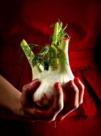 Photo for Fennel in the hands of a woman on a red background. Halloween style. Spooky because fennel looks like heart with blood. - Royalty Free Image