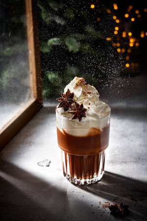 Foto de Un vaso de chocolate caliente con crema batida. Nieve de azúcar en polvo. Luces de Navidad. Acogedor invierno naturaleza muerta. - Imagen libre de derechos