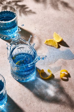 Photo for Blue colour drink garnished with sugar on the rim and lemon. Summer vibes. Hard light and hard shadows. minimalistic composition. Three cocktails in glasses. One cocktail is splashing. - Royalty Free Image