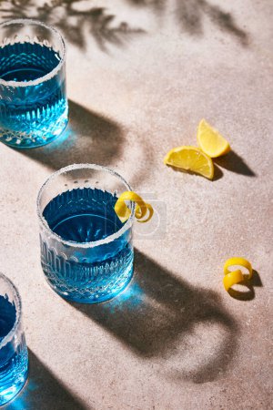 Photo for Blue colour drink garnished with sugar on the rim and lemon. Summer vibes. Hard light and hard shadows. minimalistic composition. Three cocktails in glasses. - Royalty Free Image