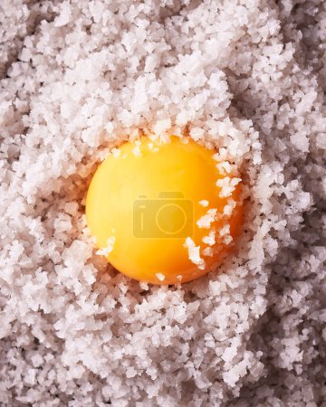 Foto de Primer plano de la yema de huevo puesta encima de la sal marina gruesa. Mucha textura. La sal está llenando el cuadro completo. Imagen vertical. - Imagen libre de derechos