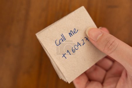 Human Connection: Offering a Phone Number.Hands deliver a message on a napkin placed on a wooden table. The note reads "call me," embodying the concept of spontaneous connections between strangers