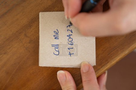 Hands write a message on a napkin placed on a wooden table. The note reads "call me," embodying the concept of spontaneous connections between strangers