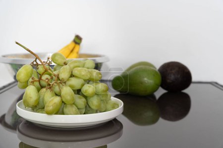 Fresh bananas, ripe avocados, and plump green grapes meticulously arranged on a sleek black table