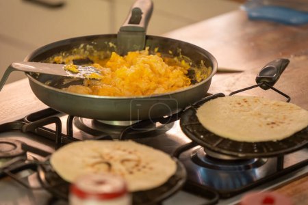 Kolumbianische Frühstücksfreude: Arepas und Rührei. Frisch gebackene Arepas brutzeln auf dem Herd, während eine Pfanne mit flauschigen Rührei wartet. Der Duft traditioneller kolumbianischer Aromen erfüllt die Luft