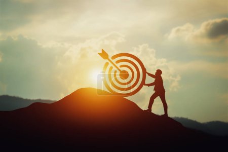 concept of business and finance. businessman standing on target on top and arrow on background of the sunset