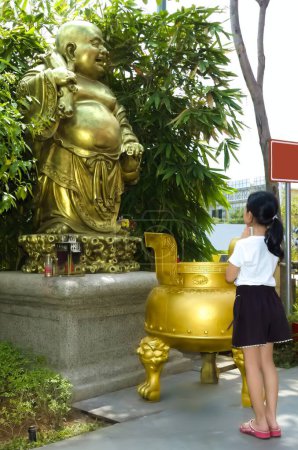 Ein kleines asiatisches Mädchen betet inbrünstig vor der Maitreya Buddha Statue