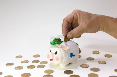 Hand putting coins into cute piggy bank with pile of coins,