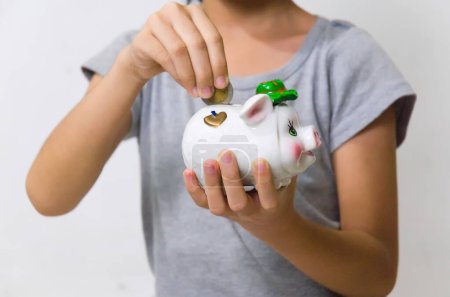 Little girl holding piggy bank and putting coins inside.