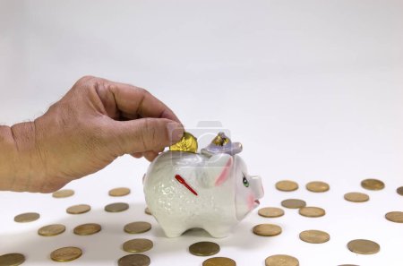 Hand putting coins into a cute piggy bank with coins scattered around it. Concept about finance and saving.