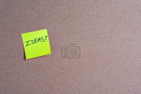 The word Ideas on a yellow sticky note posted on a corkboard