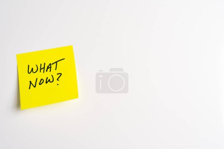 The words What Now on a yellow sticky note posted on an isolated white background