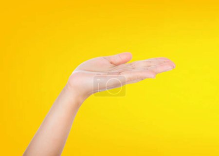 Foto de Una poderosa mano masculina con una palma extendida presenta simbólicamente un producto imaginario en un concepto publicitario dirigido a las mujeres. La escena está aislada sobre un vibrante fondo amarillo. - Imagen libre de derechos