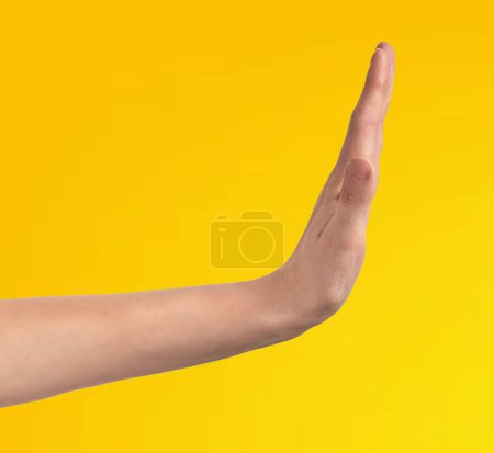 Foto de Primer plano: La mano de un hombre fuerte haciendo un gesto de stop, aislado sobre un fondo amarillo - Imagen libre de derechos