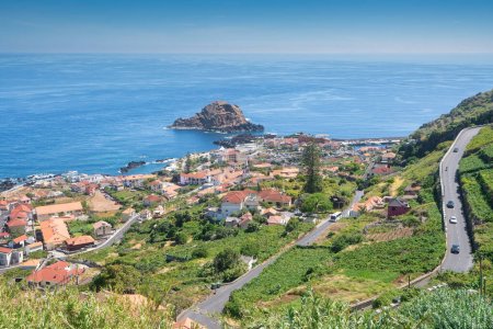 Ein Blick auf die Hafenstadt auf der Insel Madeira an einem schönen sonnigen Tag. Auf dem Foto sieht man den Ozean, die aus dem Wasser ragenden Felsen, die Kirche und die Häuser.