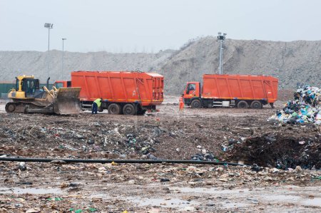 Foto de Vaciar residuos municipales. Trabajadores con camiones y excavadoras en el trabajo en vertederos de almacenamiento de residuos. - Imagen libre de derechos