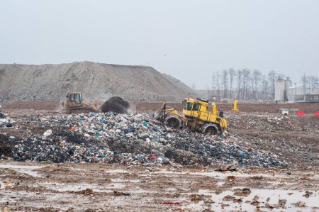 Dump municipal waste. Workers with trucks and bulldozers at work in waste storage landfill.