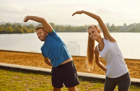 Téléchargez les photos : Jeune en forme et couple actif faisant du sport étirement exercice dans la nature. Heureux homme et femme souriants en tenue de sport qui s'entraînent dans le parc. Concept d'entraînement en plein air et de fitness. - en image libre de droit
