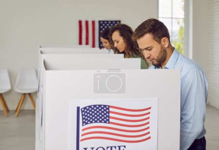 Foto de Ciudadanos estadounidenses ciudadanos estadounidenses votantes de pie en una fila en el centro de votación con nosotros banderas que van a poner sus boletas en la cabina de votación. Concepto de democracia y día electoral. - Imagen libre de derechos
