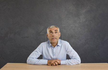 Pensive middle-aged Caucasian man sit at desk look up blank empty copy space think make decision. Mature male consider good sale promotion deal or discount offer, plan or contemplate idea.