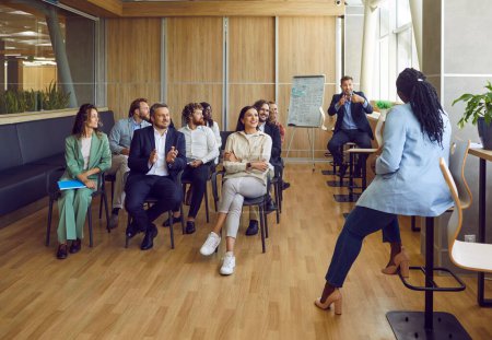 Photo for Group of diverse people on meeting discussing work project or having business training sitting in a row in office. Company employees listening to their colleague with a report in conference room. - Royalty Free Image
