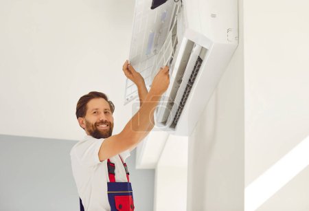 Photo for Portrait of smiling male technician in work uniform installing or repairing air conditioner. Technician is installing air conditioning equipment with screwdriver. Concept of technician service. - Royalty Free Image