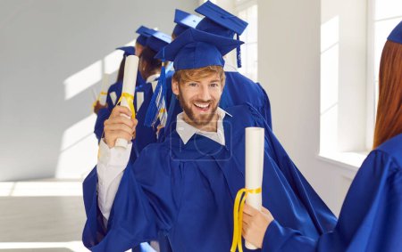 Foto de Hombre graduado de una universidad o academia lleva mortero y vestido, con diploma. Rodeado de estudiantes, irradia alegría, marcando un momento en la escuela secundaria o viaje a la universidad para obtener un título. - Imagen libre de derechos