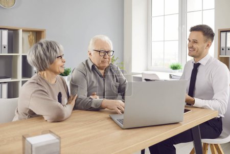 Photo for Smiling happy elderly couple talking with man advisor about health insurance or investments sitting at the desk in office with laptop. Senior man and woman talking with male financial agent. - Royalty Free Image