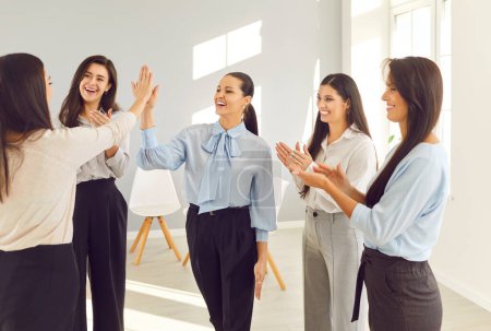 Téléchargez les photos : Au bureau, un groupe diversifié de femmes sourit alors qu'elles applaudissent et échangent cinq voix, célébrant le succès de l'équipe. Réalisation au sein de l'équipe d'affaires, pouvoir de collaboration et de soutien. - en image libre de droit