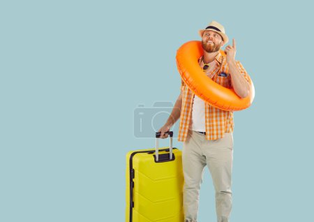Hombre feliz en ropa de vacaciones brillante con maleta lista para el viaje de verano, anillo inflable de goma alrededor del cuello. Soñar con el ocio, la recreación, viajar, feliz de disfrutar del descanso, emociones agradables, recuerdos