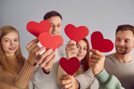 Concepto de fondo con el grupo de jóvenes adultos felices hombres y mujeres con bonitas tarjetas de papel en forma de corazón rojo en las manos, compartiendo emociones positivas y deseando que encuentre el amor en el Día de San Valentín
