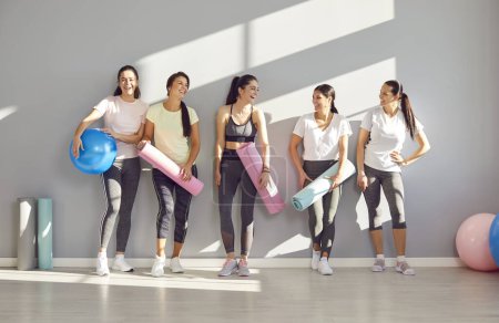 Photo for Group of young sporty girls, attractive slim happy people posing in fitness club, sportswomen team holding yoga mats. Active friends exercise or sport instruction, recreational activity together - Royalty Free Image