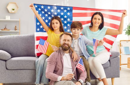 Téléchargez les photos : Bonne famille se réunit sur le canapé à la maison, orné de drapeaux des États-Unis, célébrer la fête de l'indépendance avec fierté patriotique. Avec la joie des citoyens américains commémorant ensemble cette journée nationale spéciale. - en image libre de droit