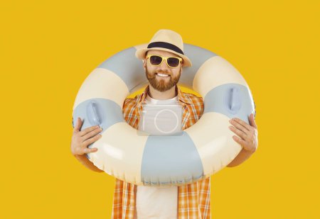Foto de Retrato de un hombre caucásico sonriente vestido de verano, sosteniendo un anillo inflable, sonriendo a la cámara sobre un fondo naranja. Él encarna la alegría de las vacaciones de verano y los viajes a la playa. - Imagen libre de derechos