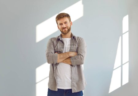Photo for Portrait of attractive smiling man standing with crossed arms. Positive handsome intelligent bearded man wearing casual clothes posing against gray wall looking at camera and smiling confidently - Royalty Free Image