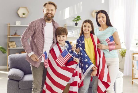 Téléchargez les photos : Famille fière souriante enveloppée dans des drapeaux américains célébrant la fête de l'indépendance à la maison. Heureuse famille de quatre personnes enveloppée dans des drapeaux américains et dégage un esprit patriotique, célébrant l'unité et la fierté nationale. - en image libre de droit