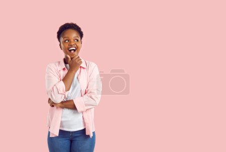 Feliz rizado rizado niña afroamericana en camisa rosa y jeans pensando mirando a un lado en el espacio de copia sobre fondo rosa. Banner para publicidad, comercialización con linda chica afroamericana.