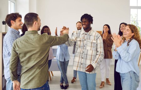 Diverse group of friends standing in a circle during meeting, expressing success. With smiles they engage in handshake or high five, creating a symbol of collaboration and teamwork.