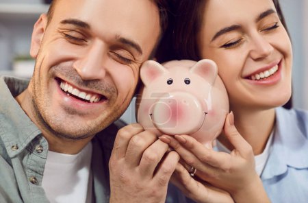 Photo for Close up of happy young family holding piggy bank indoors to save money for future. Married couple planning saving their budget together. Investments and financial freedom concept. - Royalty Free Image