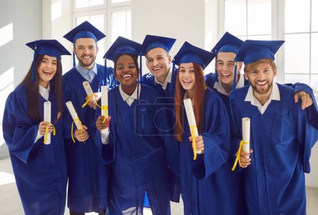 Photo for Diverse group of high school graduates, adorned in mortarboards and gowns, proudly display diplomas. This image reflects accomplishment of a multinational team of students from an esteemed academy. - Royalty Free Image