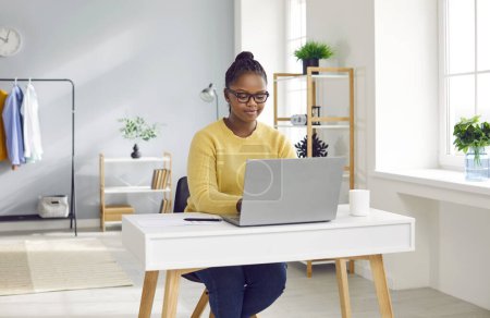 Téléchargez les photos : Portrait d'une jeune femme d'affaires brune afro-américaine travaillant avec un ordinateur portable à la maison ou à l'ofiice et la dactylographie. Comptable pigiste envisageant de nouveaux projets, analysant l'entreprise. - en image libre de droit