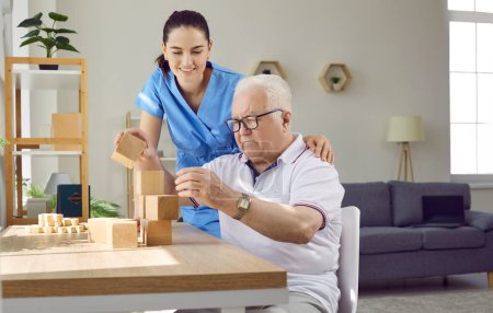 Helpful nurse playing games with old male patient. Senior man with cognitive disorder building wooden block tower while sitting at table in retirement home. Dementia care, Alzheimers disease concept