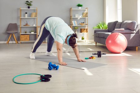 Photo for Fat, chubby, overweight, plus size, young woman doing fitness exercises on a rubber sports mat during her weight loss fitness workout in the living room at home - Royalty Free Image