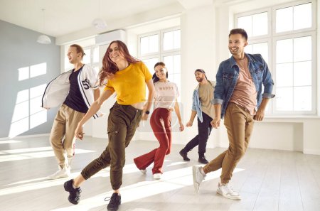 Foto de Grupo de jóvenes felices disfrutando de una clase de danza contemporánea. Equipo de alegres bailarines sonrientes en ropa casual practicando un nuevo coreo y pasándolo bien juntos en un estudio moderno - Imagen libre de derechos