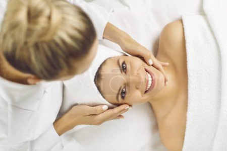 Portrait of happy woman indulges in facial massage by a cosmetologist in beauty salon. Conveying tranquility and expert spa care, showcasing the woman serene expression during the procedure.